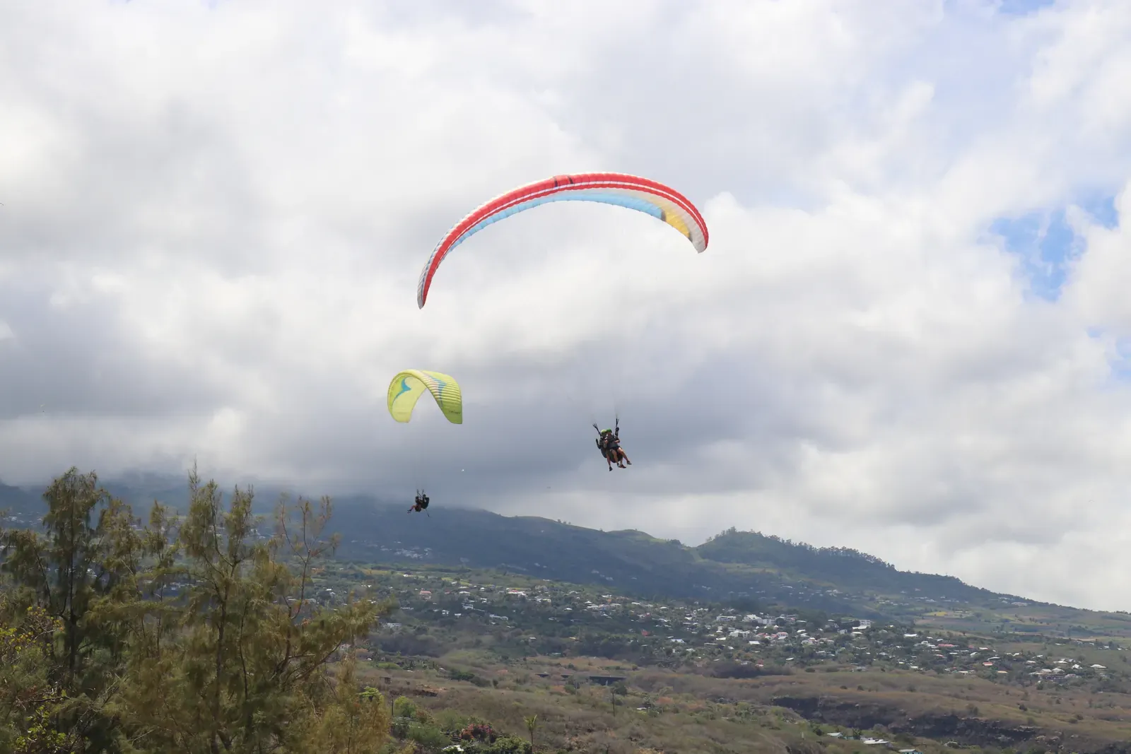 Deux parapentes en vol au-dessus des pentes boisées, sous un ciel de nuages