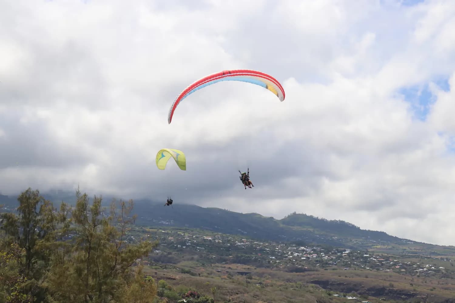 Paragliders flying in a cloudy sky above the wooded heights of the west